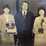 An old photo of two women with their trophies and a man in the middle