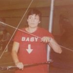 An old photo of a female athlete with a red shirt that reads \"Baby\" with an arrow pointing downwards