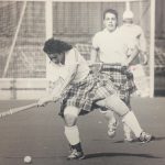 An old photo of a female field hockey player about to hit a ball