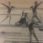 An old photo of gymnasts posing by a balance beam