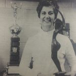 An old photo of Mary Lyons smiling at the camera while holding a trophy