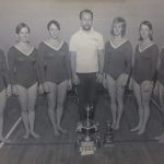 An old photo of female gymnasts with their coach and trophies