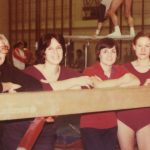 Female Gymnastics athletes and coaches smiling at the camera by a balance beam