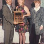 A female athlete holding a perpetual plaque and posing for the camera with two other people at Banquet of 1996-97