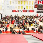 A shot of students sitting in circles taken from the top the gym seating
