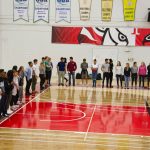 An overhead shot of students lined up by the white perimeter marked on the gym floor