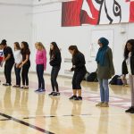 Students lined up along the basketball court perimeter for a long jump activity