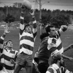 Group of rugby players, one of whom is jumping up to catch a ball