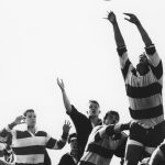 Group of rugby players reaching and jumping up to catch a ball in the air
