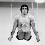 An old photo of a male gymnast doing ring pull-ups